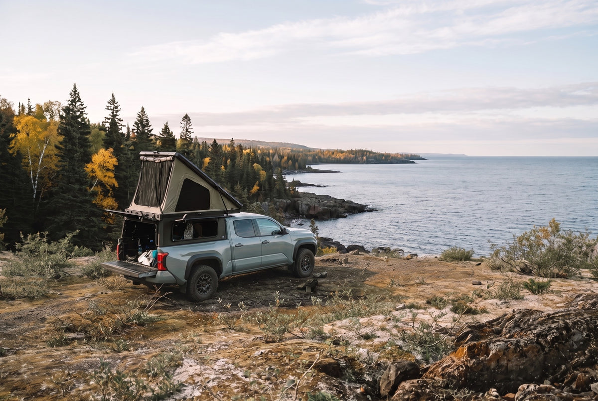 Wide view of a Toyota Tacoma truck camper set up above the Lake Superior shoreline in autumn