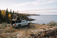 Wide view of a Toyota Tacoma truck camper set up above the Lake Superior shoreline in autumn