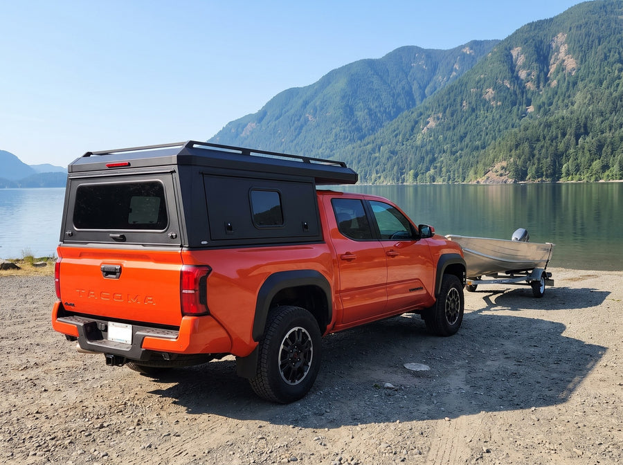 Toyota Tacoma with a windowed truck cap towing an aluminum fishing boat at a boat launch