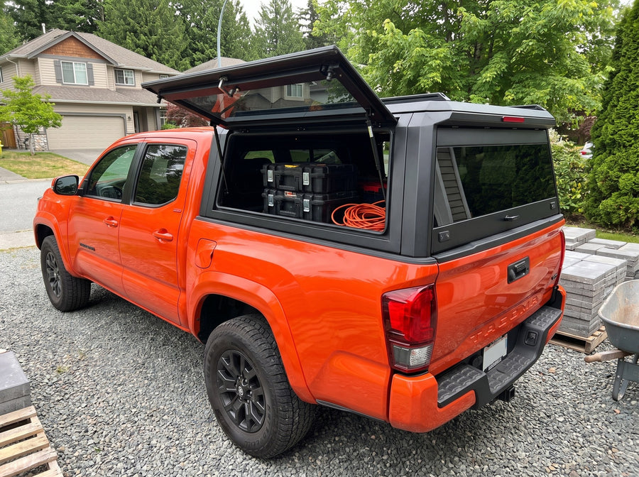 Toyota Tacoma truck cap with the side window lifted open at a job site, tool cases and an extension cord inside