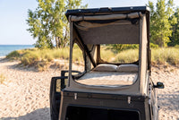 Rear view of the Toyota Tundra truck cap camper with the large rear tent window open and the bed made, on a Lake Huron beach