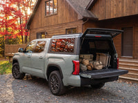 Toyota Tundra truck cap open at a cottage with duffel bags, a cooler and a camp chair packed in the bed