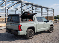 Toyota Tundra truck cap with the side window lifted open at a job site, tool cases and an extension cord inside