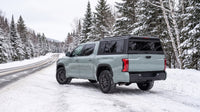 Wide view of a Toyota Tundra with a windowed aluminum truck cap parked at a snowy two-lane road through the Laurentian mountains of Quebec in winter