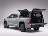 Rear door of the Toyota Tundra truck cap lifted open with the tailgate down and storage totes in the bed