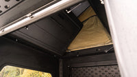 Inside the aluminium truck canopy showing the hinged bed panel, gas struts and perforated MOLLE wall