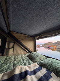 Waking up in the truck cap camper roof tent: quilted bedding and an open window over a quiet fishing cove