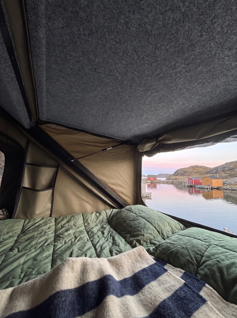 Waking up in the truck cap camper roof tent: quilted bedding and an open window over a quiet fishing cove